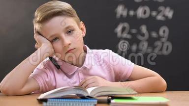 上数学课的时候，一个无聊的小男孩坐在<strong>课桌</strong>前看着摄像机
